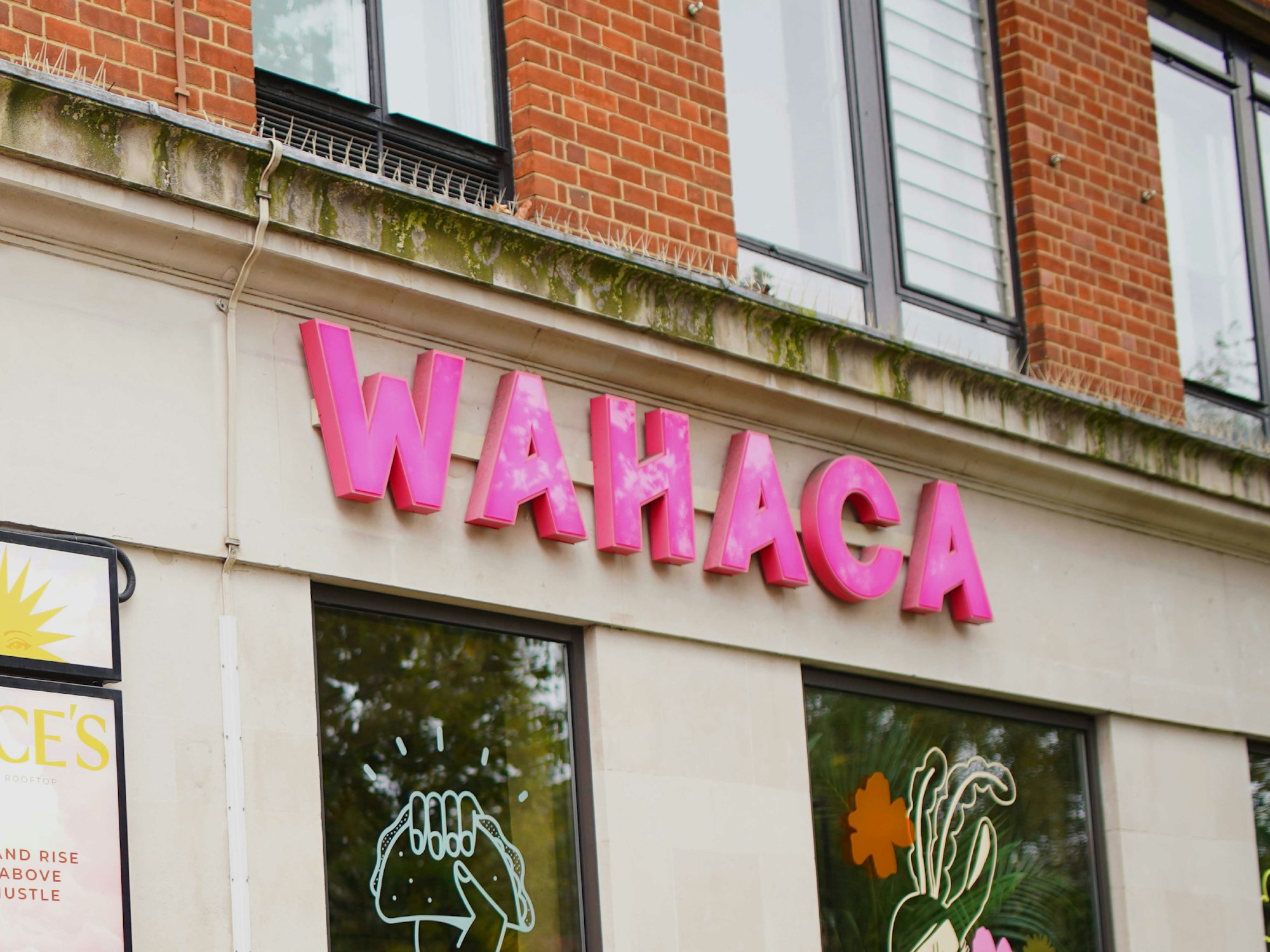 A restaurant building with a visible pink sign labeled "Wahaca," attached to the exterior wall.