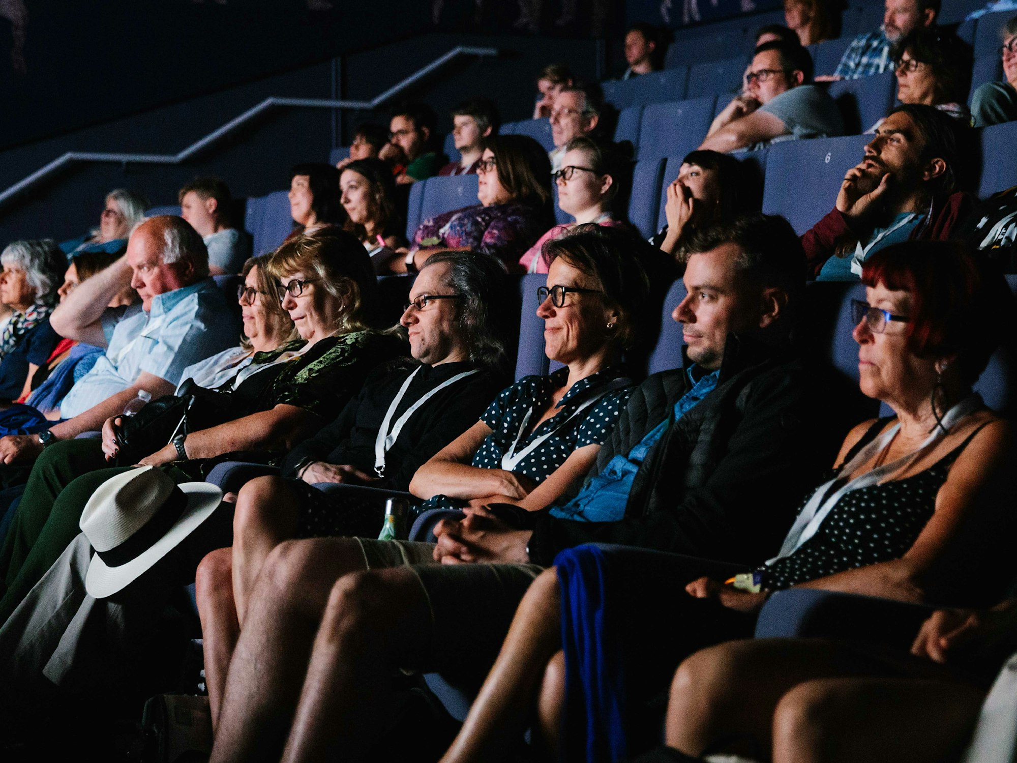 Audience members seated in a dimly lit theater, attentively watching a presentation.