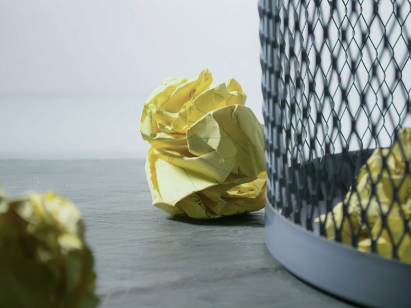 Crumpled up balls of paper surround a mesh mixed recycling metal bin in an office. Some pieces have successfully made it inside the bin.