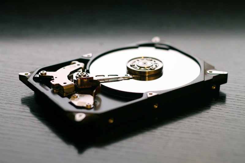 Black desktop table with an open hard rive placed on top. The internals of the hard rive are exposed with a view into the disc and needle.