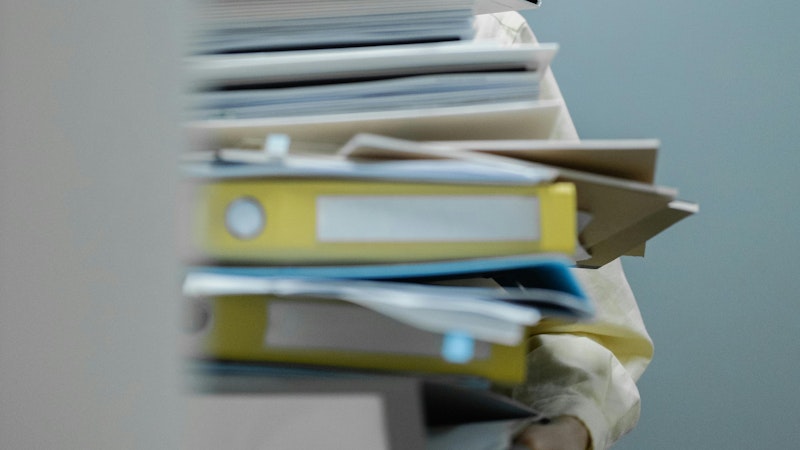 Pile of untidy yellow lever arches and paper being held up by a man.