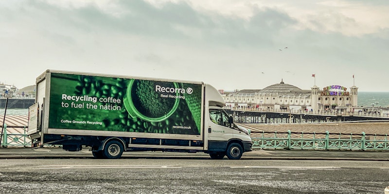A Recorra truck is parked near the Brighton pier and promenade. In the background, a pier and overcast sky are visible.